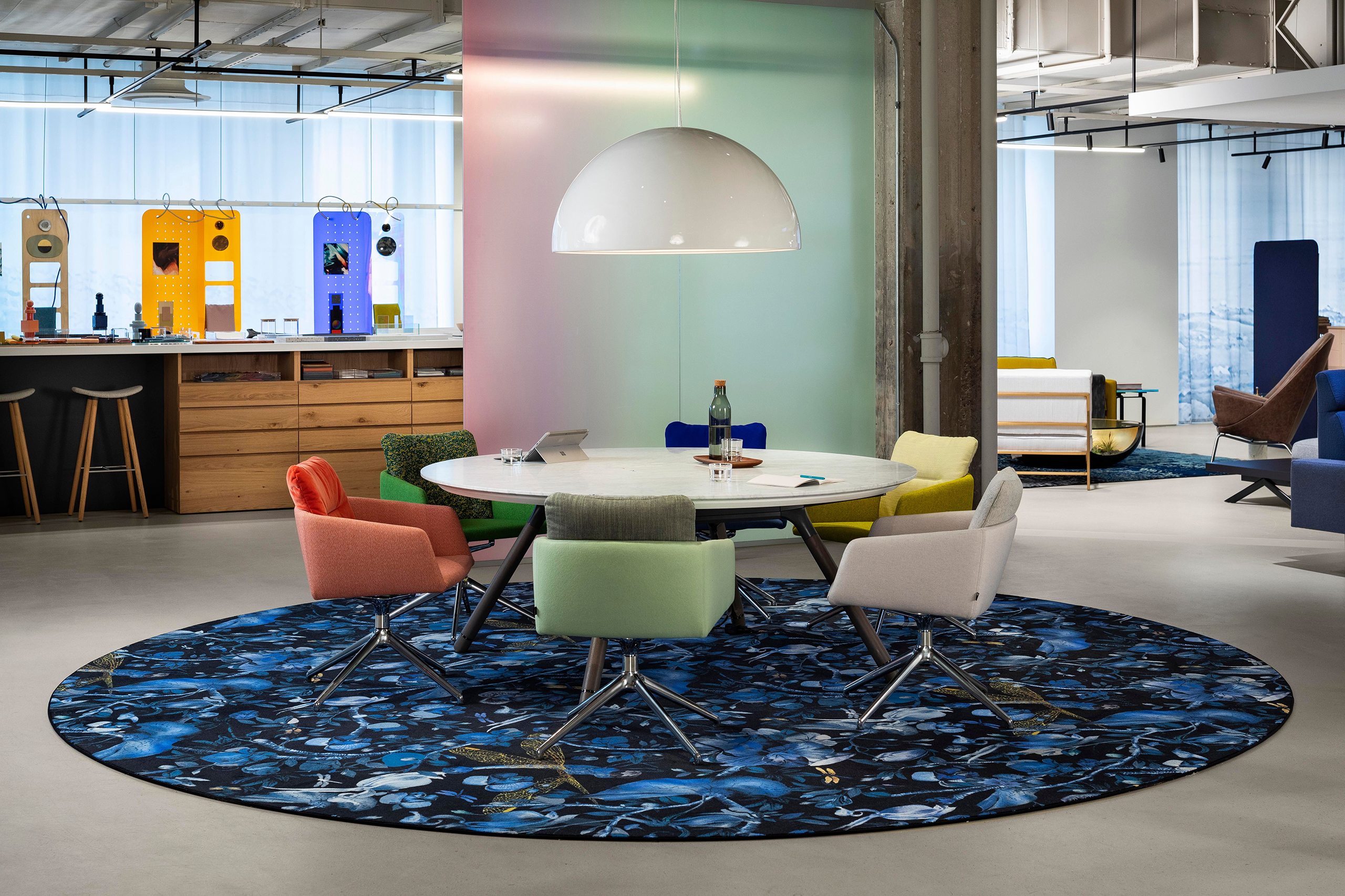 Round meeting table surrounded by colorful chairs on a circular patterned rug