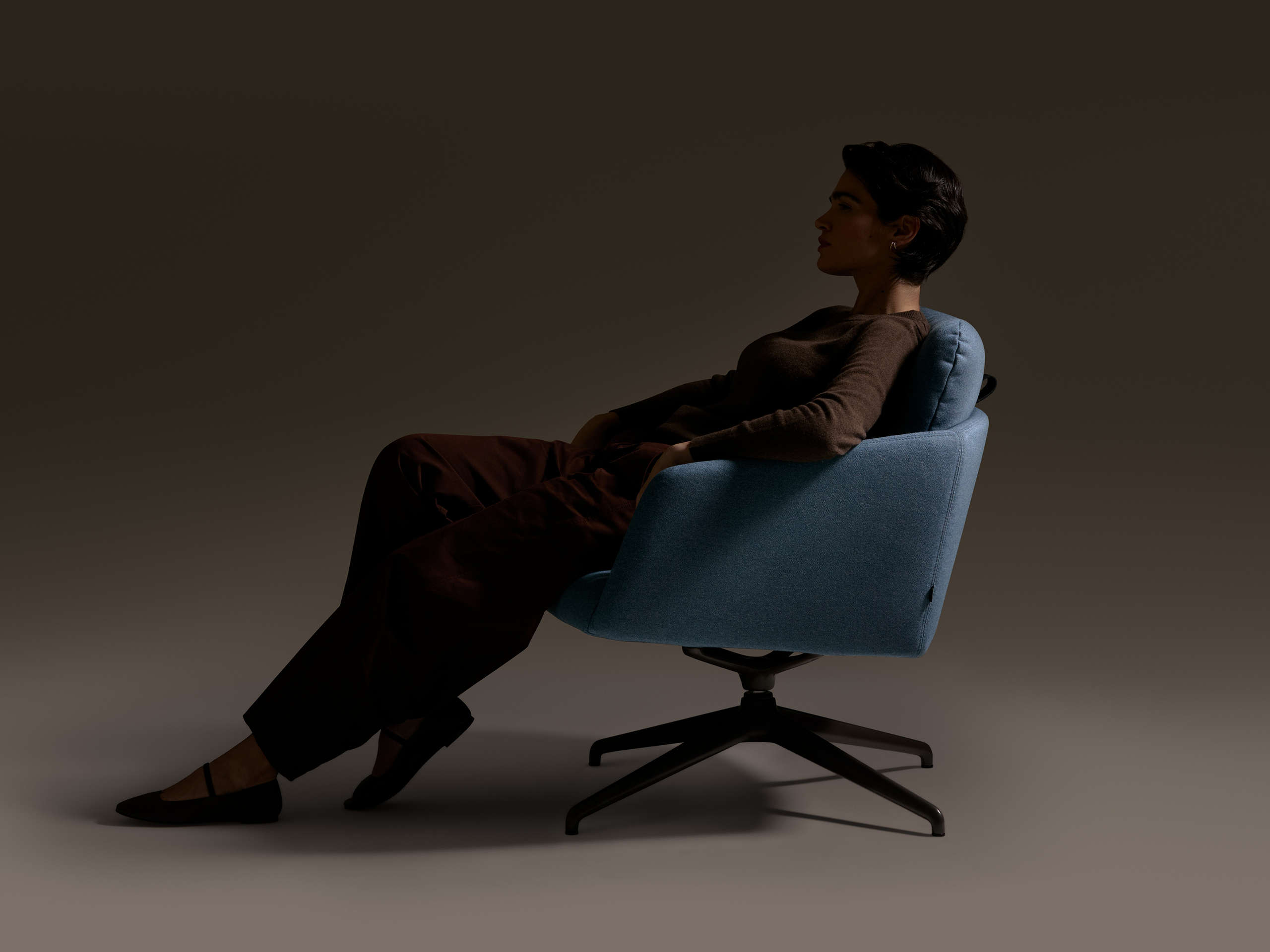 Side view of a person reclining in a blue upholstered lounge chair against a neutral background.