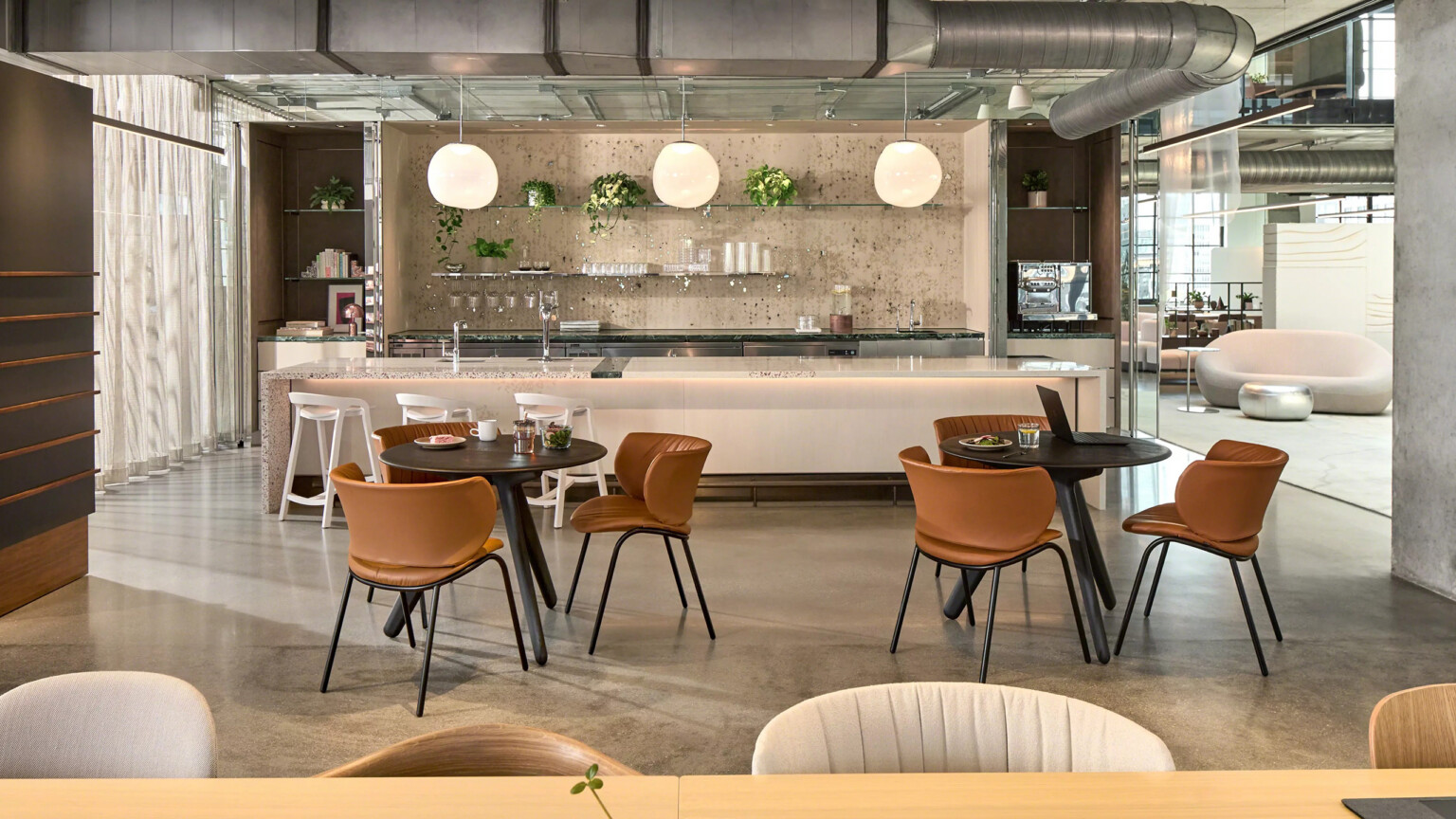 Modern café interior space with round tables, leather chairs, and a central bar beneath hanging globe lights.