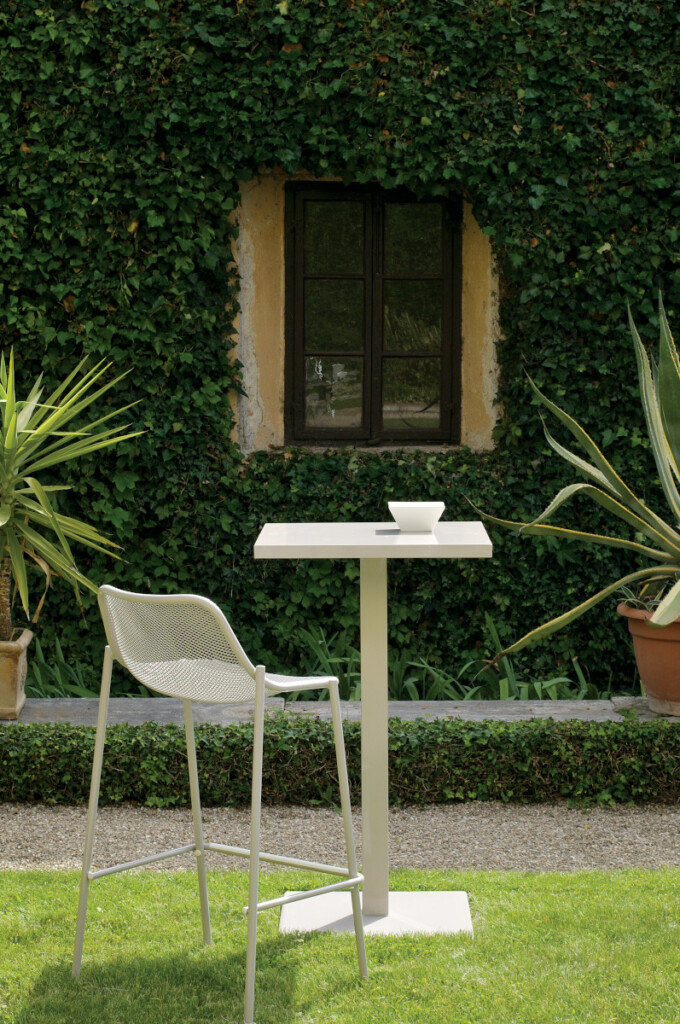 White table and stool set on a lawn in front of an ivy-covered wall.