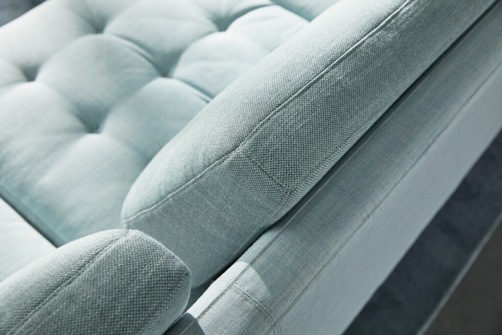 Close-up of light blue upholstered sofa with tufted seat and textured fabric