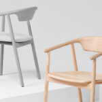 Two armchairs shown on white platforms, one in light gray with a white seat cushion and one in natural wood.