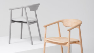 Two armchairs shown on white platforms, one in light gray with a white seat cushion and one in natural wood.
