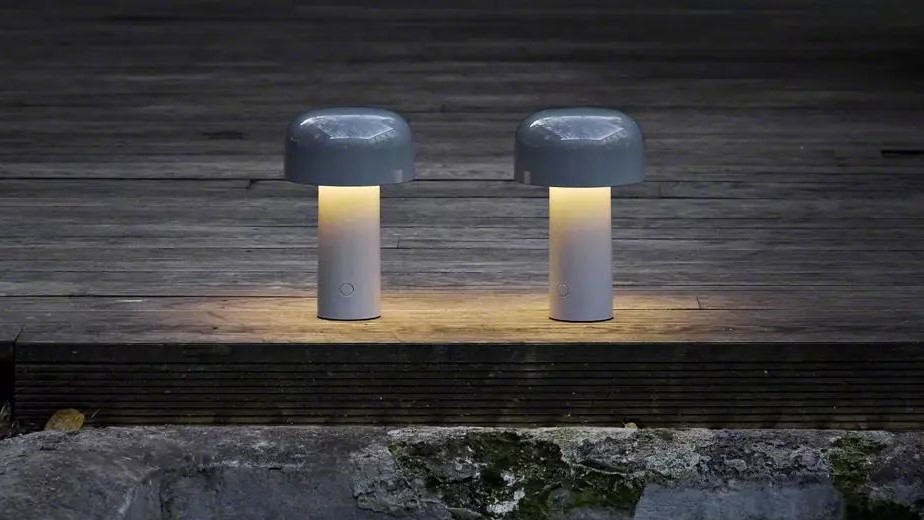 Two small cylindrical outdoor lamps placed side by side on a wooden deck at night
