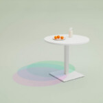 Round white pedestal table on a light green background with a small plate of oranges and a bottle on top.