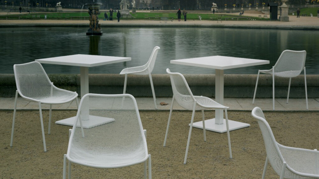 White outdoor chairs and square tables beside a garden setting