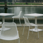 White outdoor chairs and square tables beside a garden setting