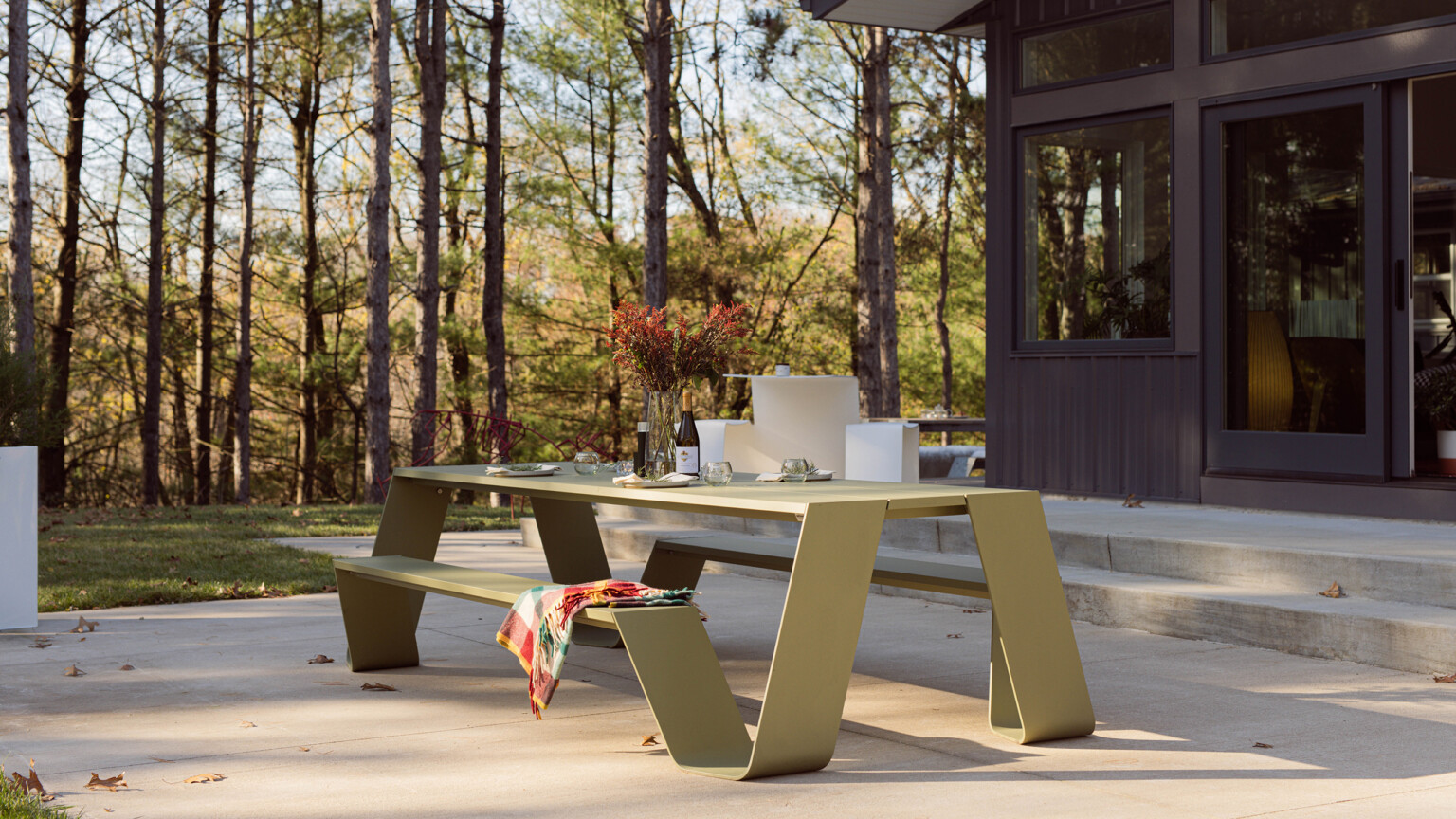 Outdoor picnic table on a patio set with tableware and surrounded by trees