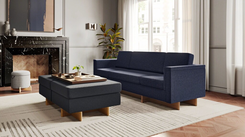 Modern living room with a blue sofa, matching ottoman, fireplace, and large windows.