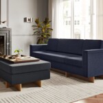 Modern living room with a blue sofa, matching ottoman, fireplace, and large windows.