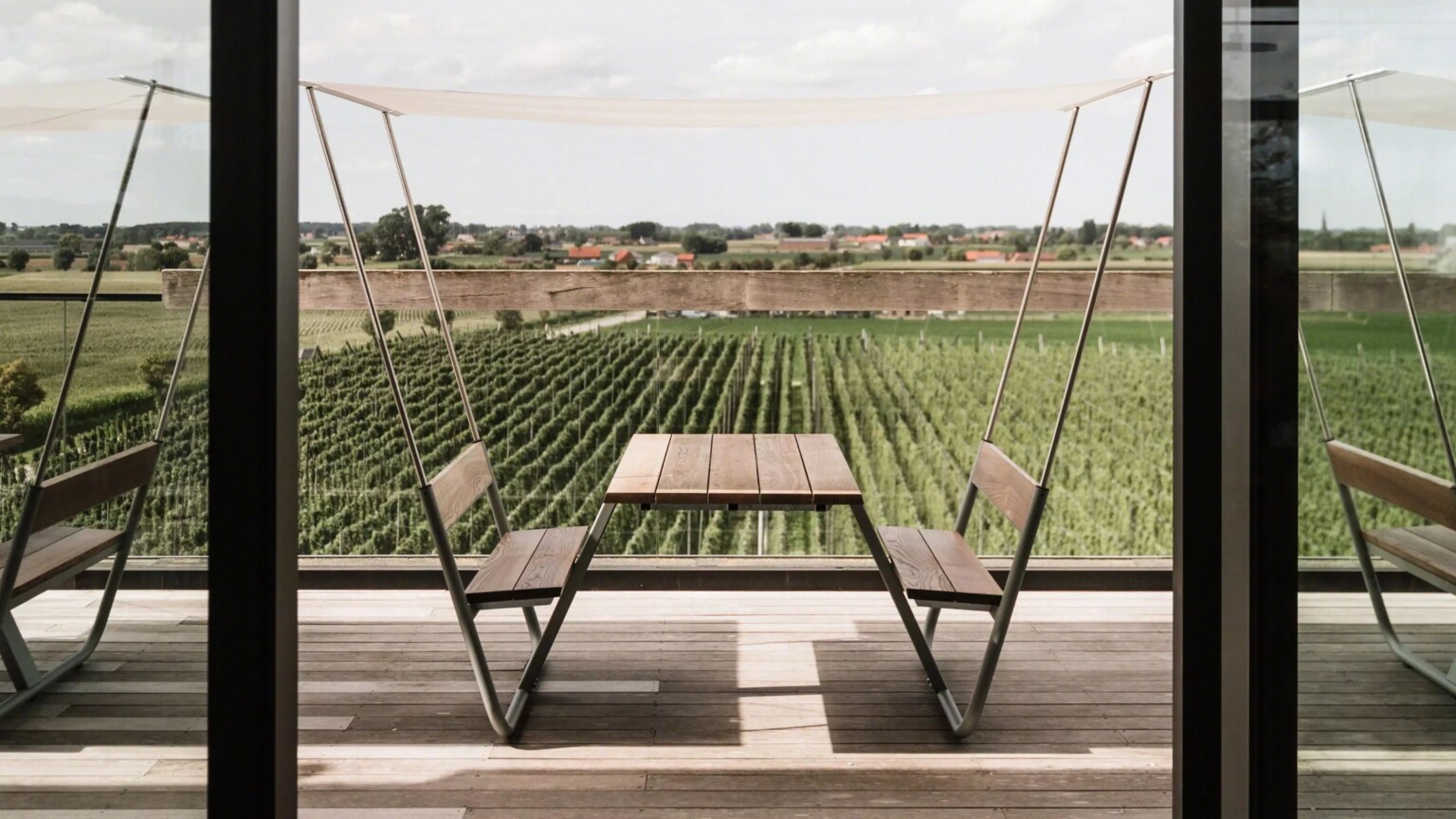 Outdoor table and bench set on a terrace overlooking green vineyards