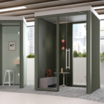 Office workspace with two enclosed acoustic booths featuring glass doors, and city views through large windows.