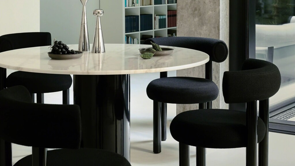 Round white marble dining table surrounded by black chairs in a modern interior space