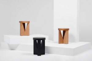 Three stools displayed on white platforms, shown in natural wood and black finishes.