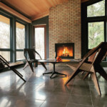 Interior living space with wooden lounge chairs, a low table, large windows, and a lit fireplace.