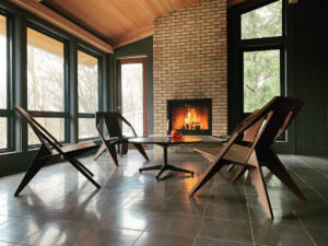 Interior living space with wooden lounge chairs, a low table, large windows, and a lit fireplace.