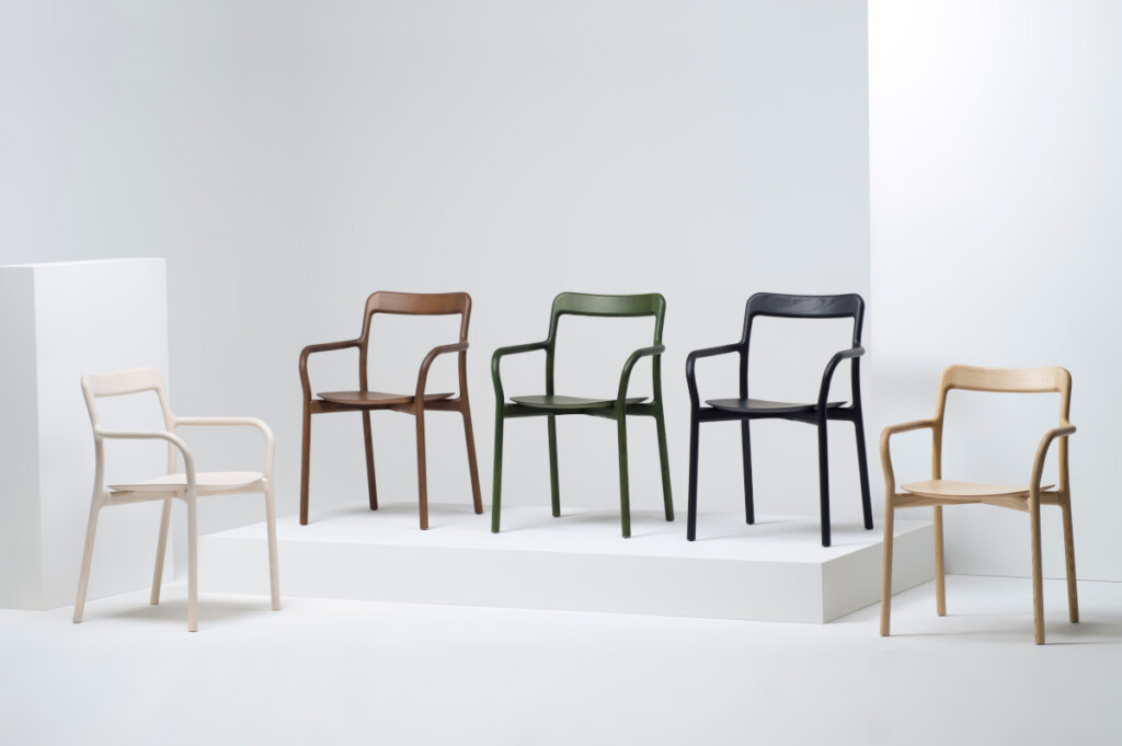 Modern armchairs displayed on white platforms, shown in white, brown, green, black, and natural wood finishes.
