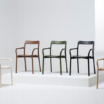Modern armchairs displayed on white platforms, shown in white, brown, green, black, and natural wood finishes.