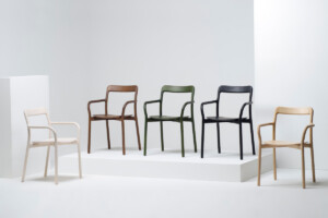 Modern armchairs displayed on white platforms, shown in white, brown, green, black, and natural wood finishes.