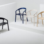 Four armchairs displayed on white platforms, shown in black, navy, white, and light wood finishes.