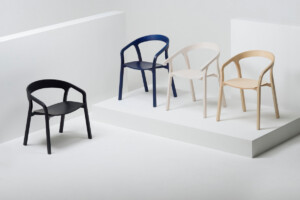 Four armchairs displayed on white platforms, shown in black, navy, white, and light wood finishes.