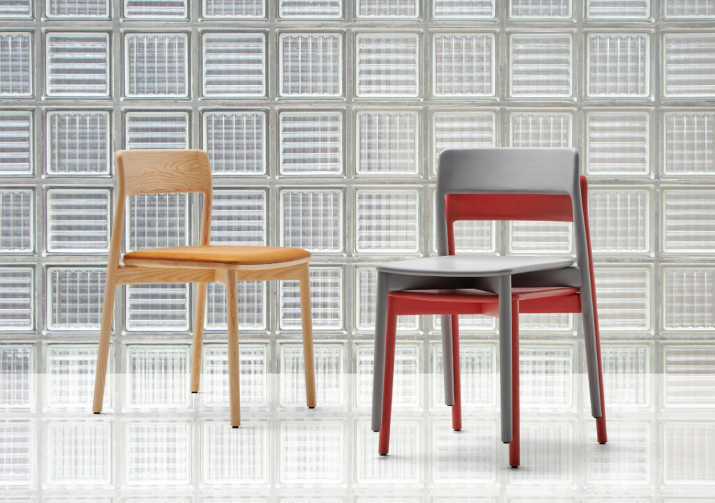Two chairs displayed in front of a glass block wall, one in natural wood with a tan seat and one in gray and red.