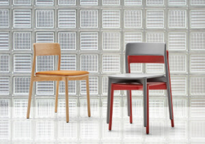 Two chairs displayed in front of a glass block wall, one in natural wood with a tan seat and one in gray and red.