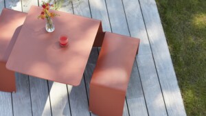 Orange outdoor table decorated with a glass and flowers with side benches on a wooden deck
