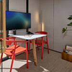 Small workspace with a white table, red chairs, a TV, and indoor plants next to a window.