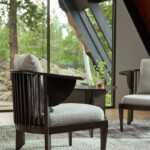 Modern lounge area with cream colored armchairs and a small side table near large windows overlooking greenery