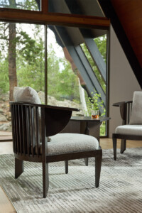 Modern lounge area with cream colored armchairs and a small side table near large windows overlooking greenery
