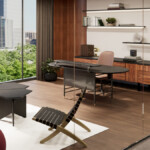Modern office-style living space with a desk, lounge seating, and large windows overlooking a cityscape and trees.