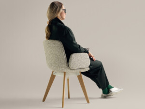 Woman seated in beige chair with wooden legs.