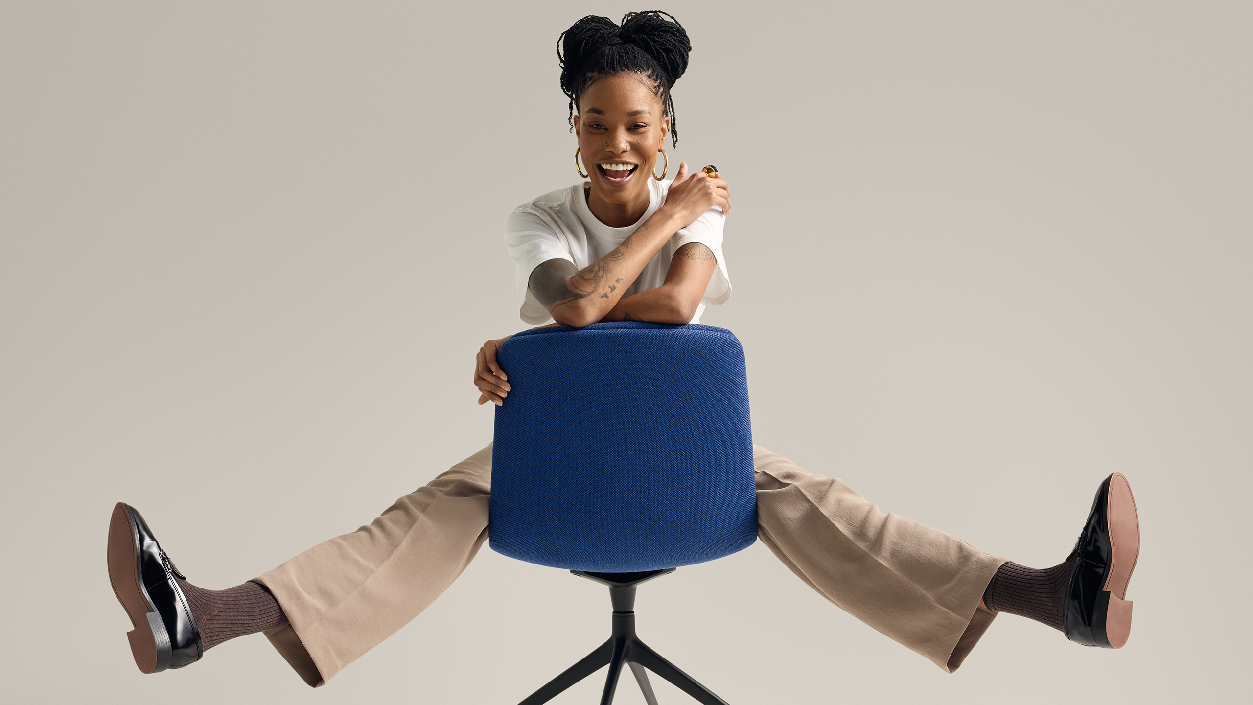 Woman seated playfully on blue upholstered chair against neutral background