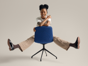 Woman seated playfully on blue upholstered chair against neutral background