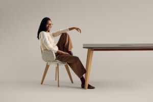 Woman sitting in upholstered chair at modern table against neutral background