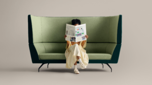 One person seated on green high-back lounge sofa reading a book against neutral background