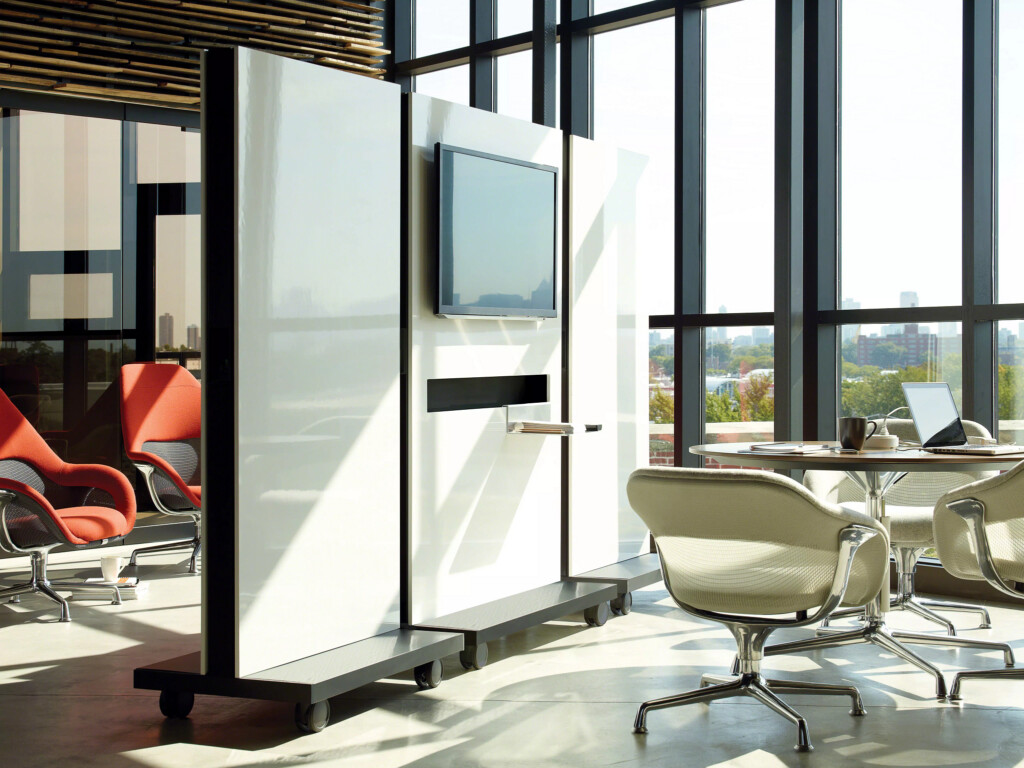 Modern collaborative workspace with mobile digital display, round meeting table, and lounge seating