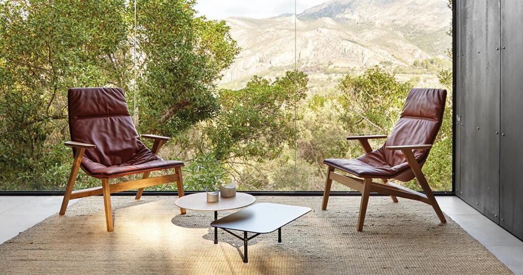Modern lounge with two red chairs, two coffee tables, and a landscape backdrop.