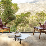 Modern lounge with two red chairs, two coffee tables, and a landscape backdrop.
