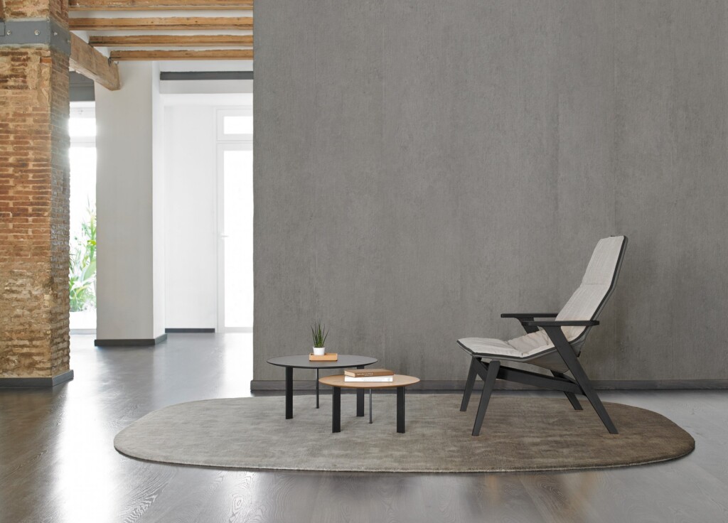 Modern lounge with a gray chair, two round tables, and a textured gray backdrop.