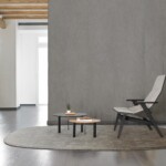 Modern lounge with a gray chair, two round tables, and a textured gray backdrop.