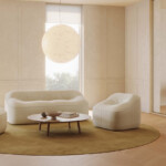 Modern lounge area with upholstered sofa, lounge chairs, round coffee table, and pendant lighting