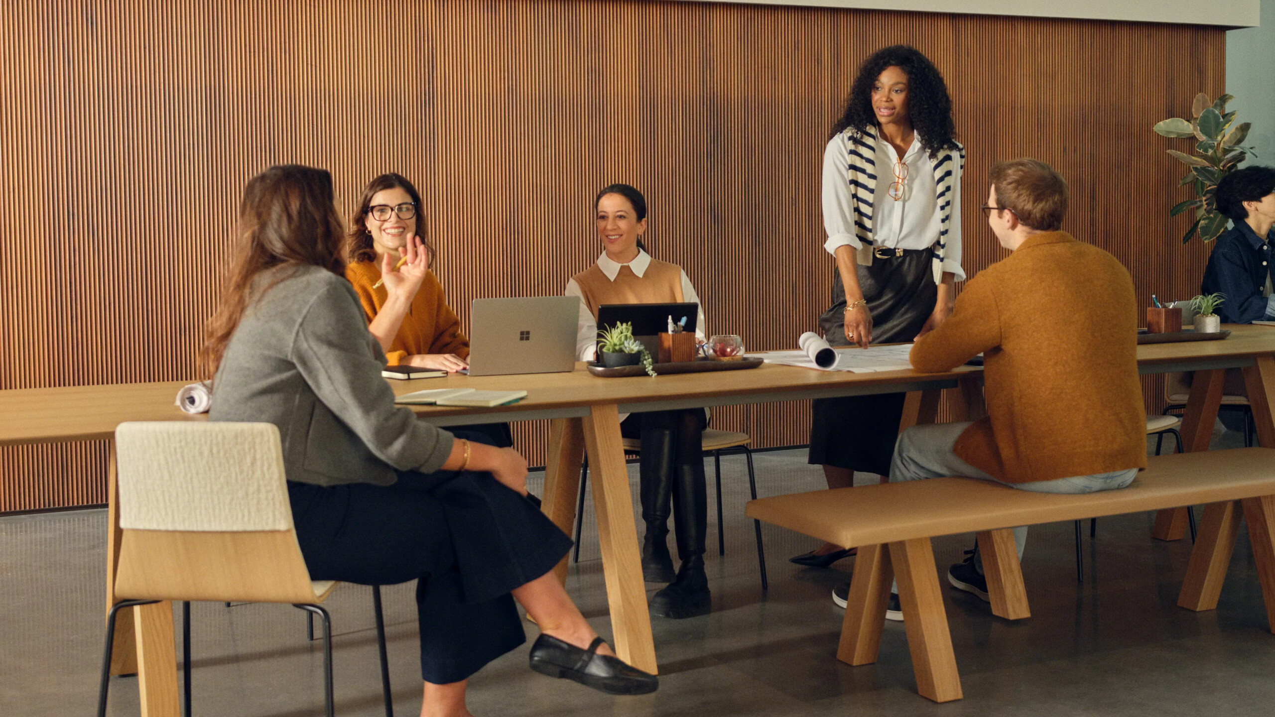 Team collaborating around wooden table in modern meeting space with laptops and documents