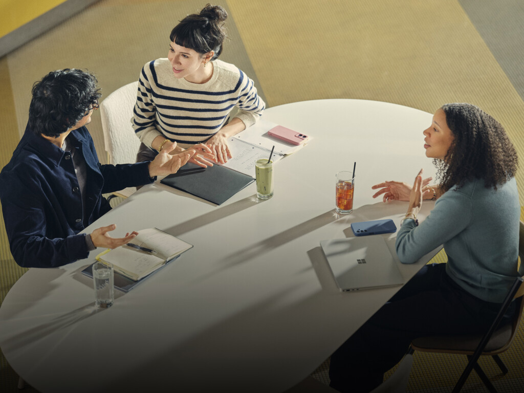 Three people collaborating at modern conference table with laptops, notebooks, and drinks