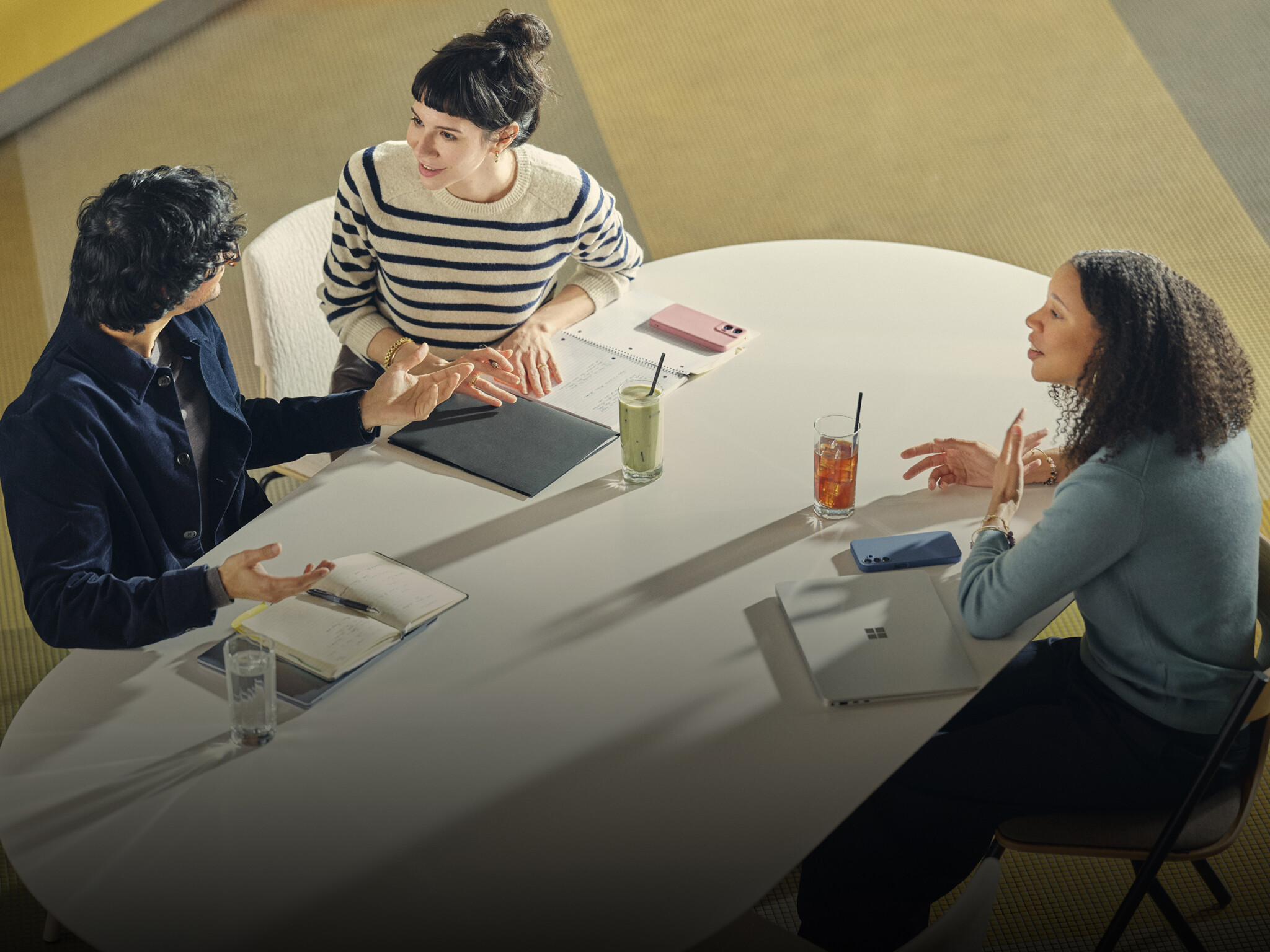 Three people collaborating at modern conference table with laptops, notebooks, and drinks