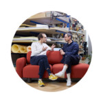 Two men conversing on red upholstered sofa in design studio with material shelving
