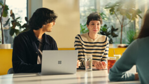 Three people seated at a table with a laptop and drinks