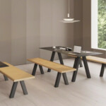 Modern interior with sets of black tables and wooden benches next to a large window showing a natural environment