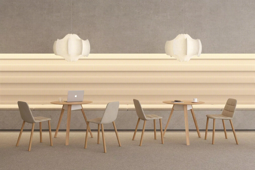 Sets of beige chairs and wooden tables in a minimalist space with modern white lamps hanging from the ceiling and an illuminated wall behind them.